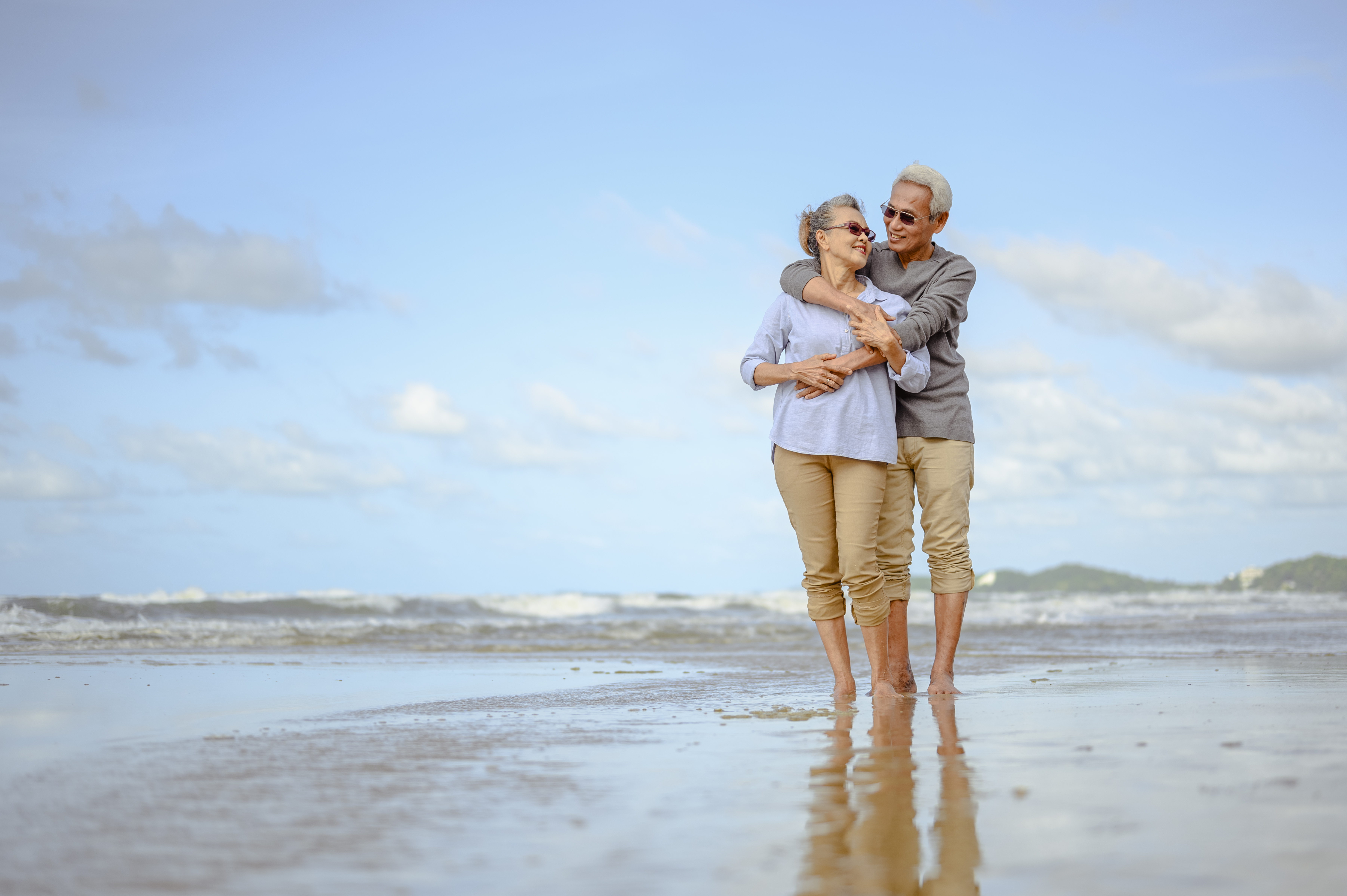 Senior couples embrace on the beach at sunny day, plan life insurance